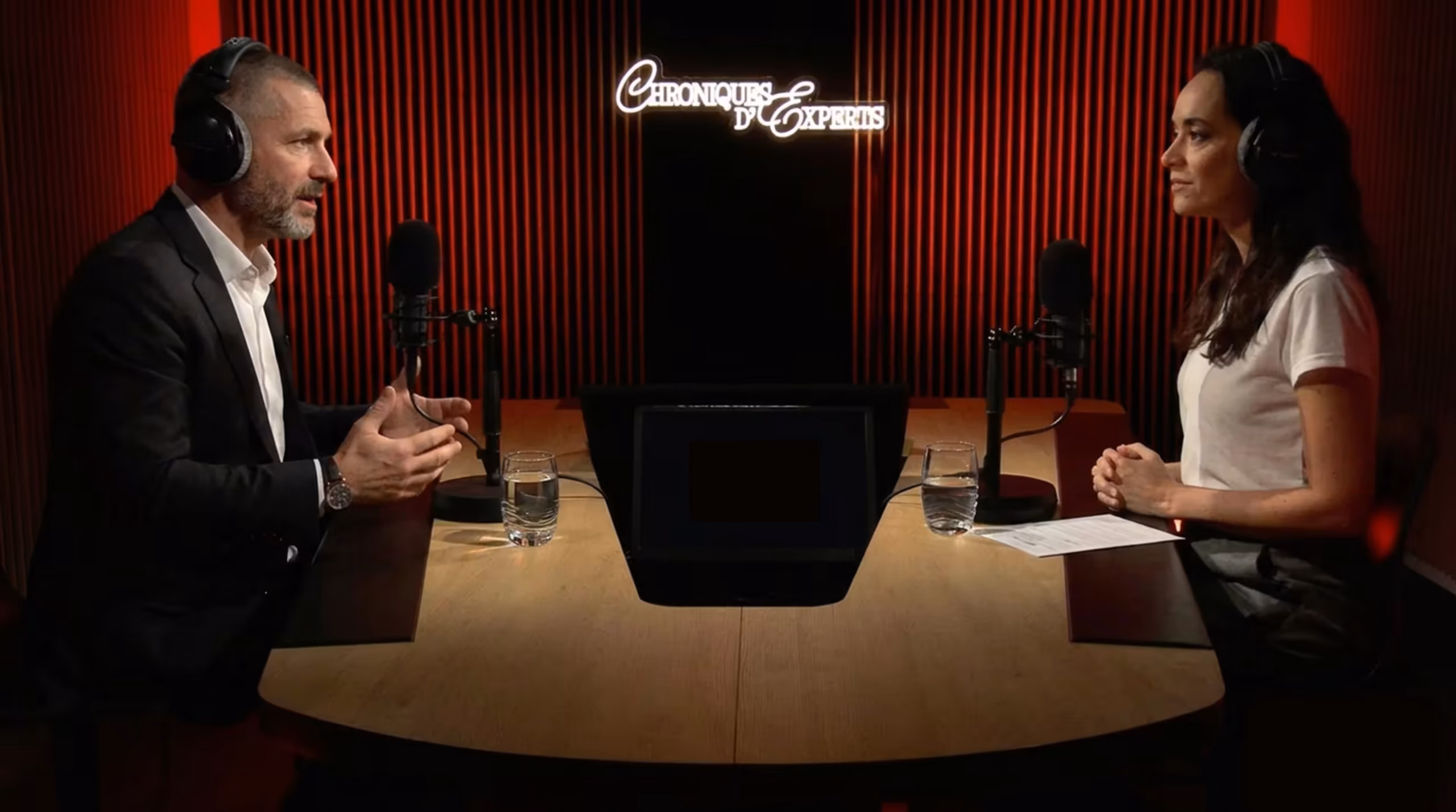Enregistrement du podcast Chroniques d'Experts au Studio Webcast, deux intervenants face à face avec casques audio et microphones sur fond de panneaux acoustiques rouges