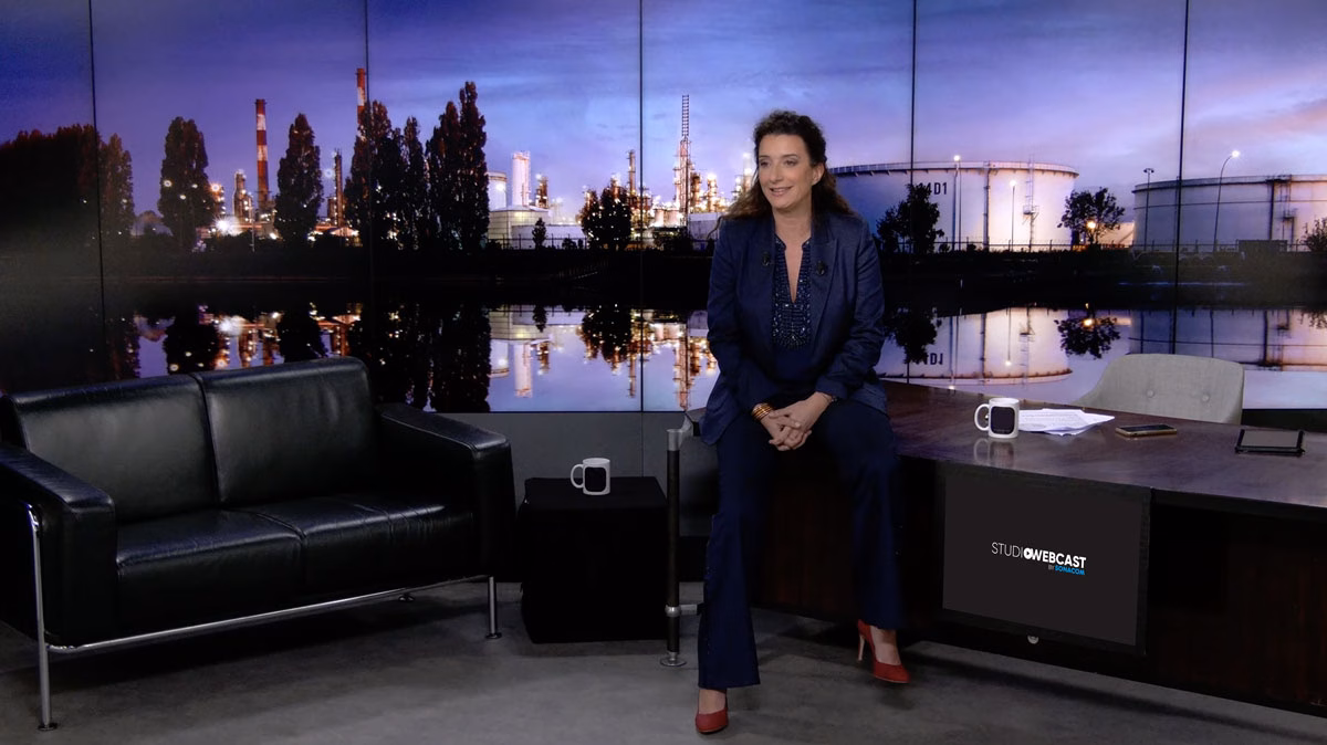 Présentatrice assise sur le bureau du plateau TV du Studio Webcast en configuration Late Show, avec canapé en cuir noir et fond de décor industriel nocturne