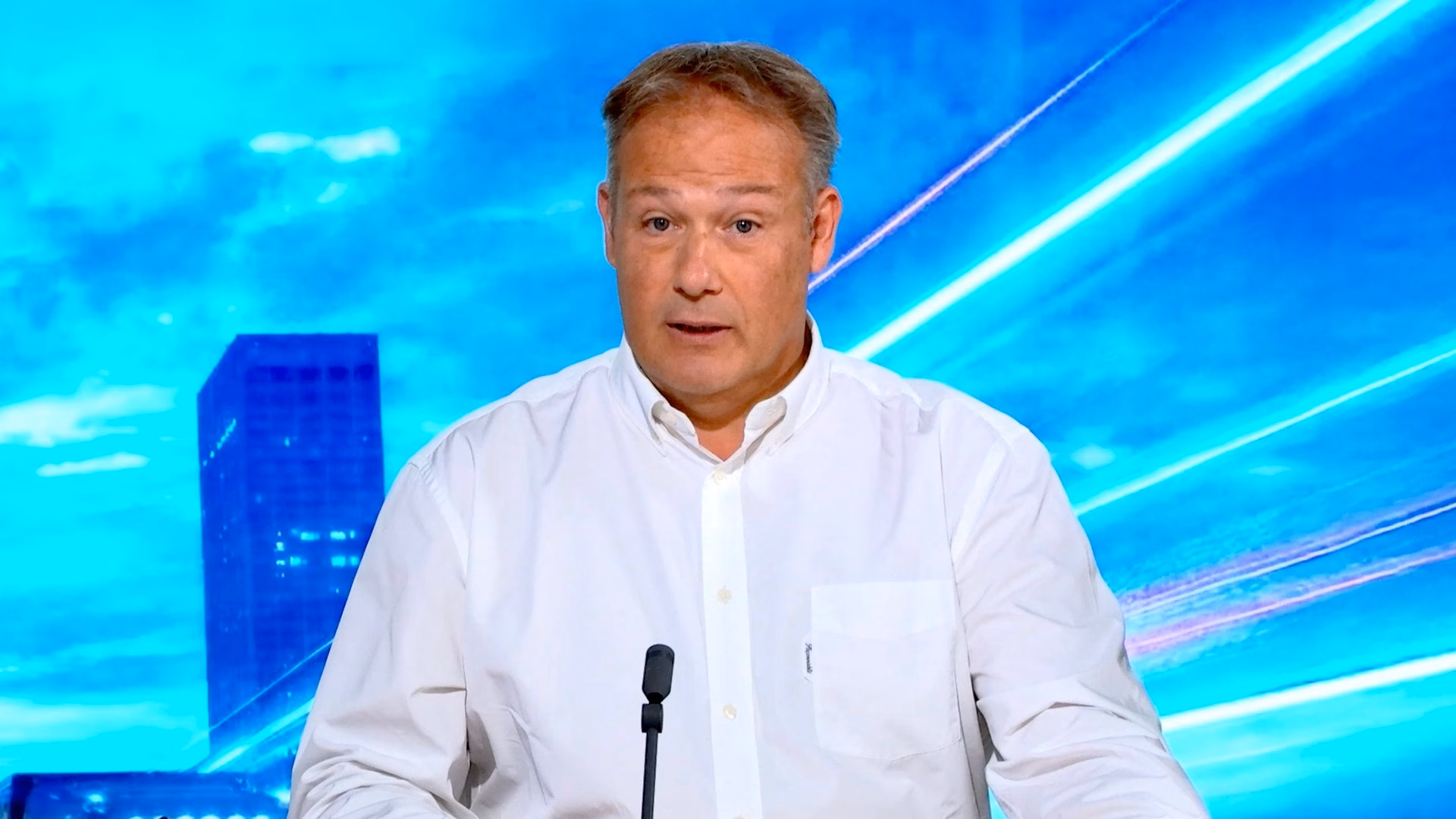 Prise de parole d'un dirigeant face caméra en plan serré, micro plateau et fond LED bleu animé — captation corporate Studio Webcast Paris.